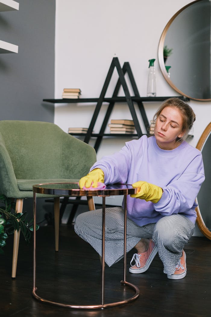 Young woman in casual attire cleaning a table with yellow gloves indoors.