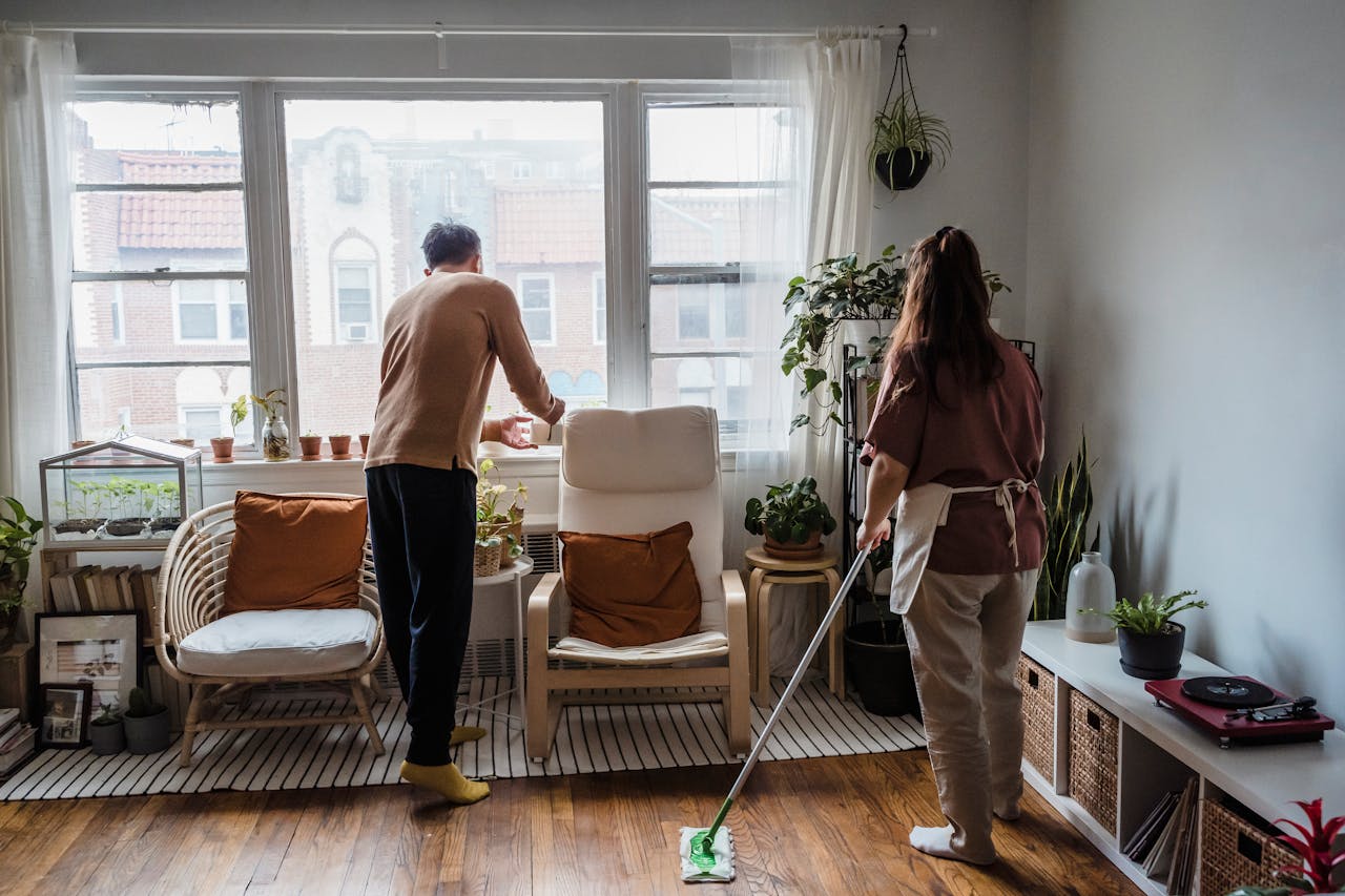 Asian couple tidying up a bright, plant-filled living room space with warm natural light.